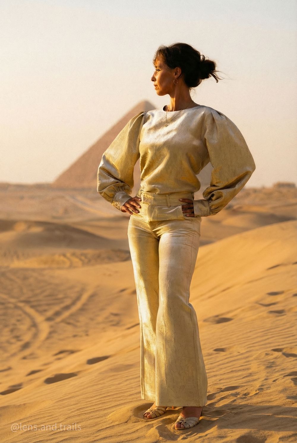 Woman in a gilded dress in the sand before the pyramid at golden hour