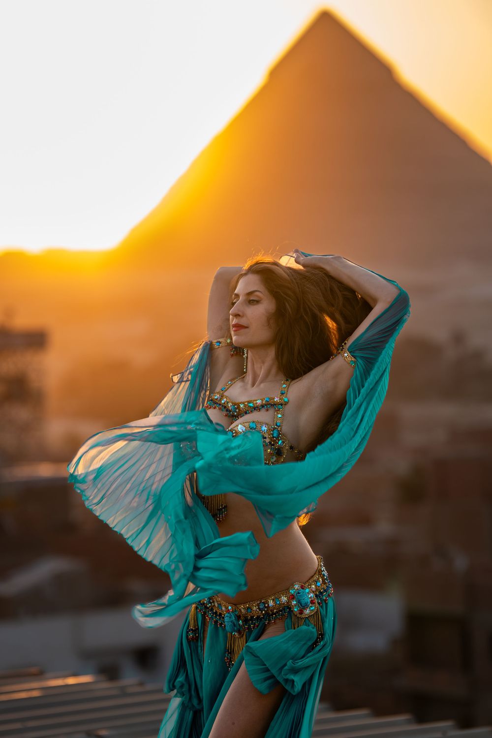 Dancer with a turquoise veil before the pyramid at dusk