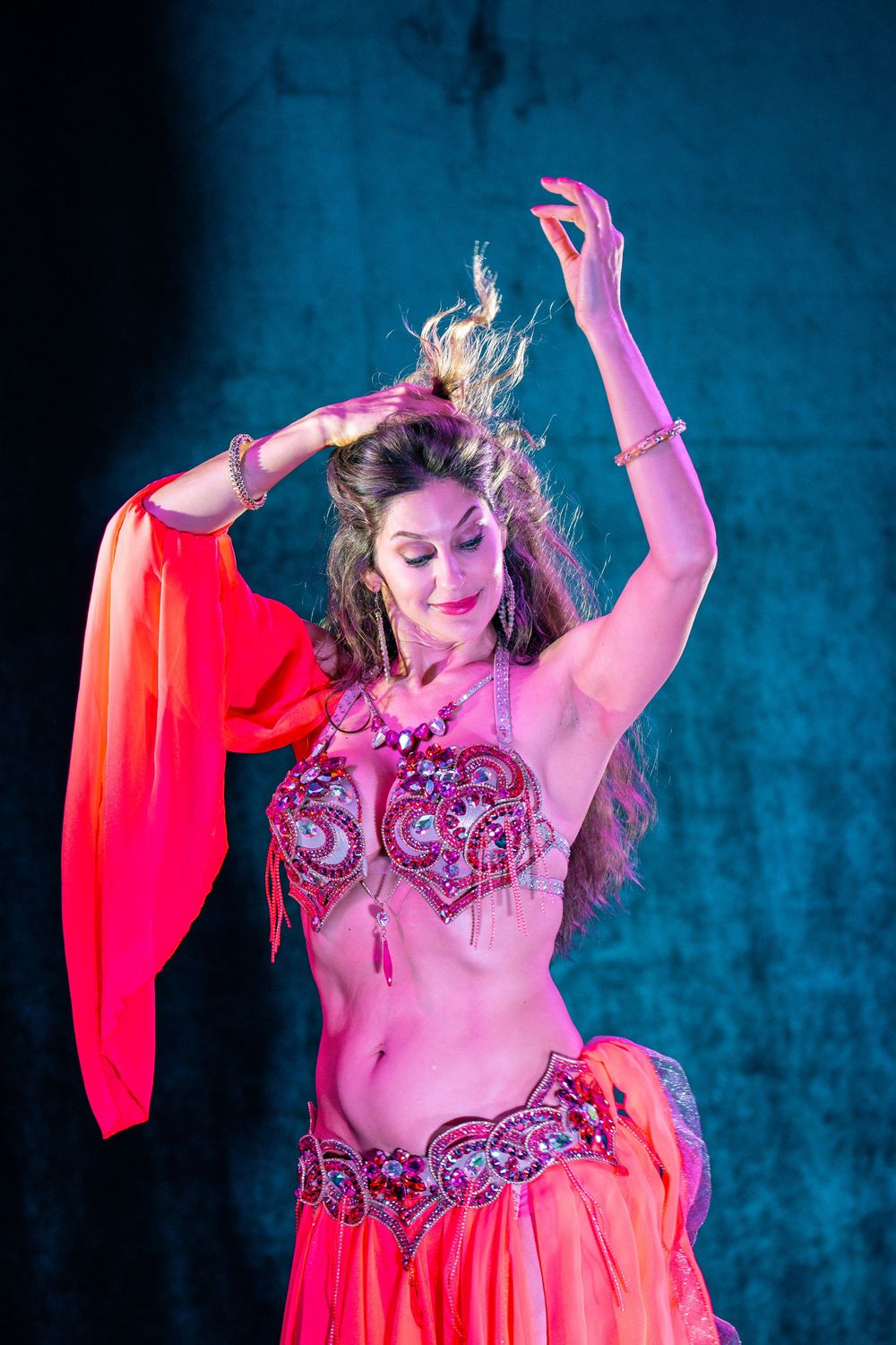 Bellydancer in amber silk on a teal-lit stage, arms raised