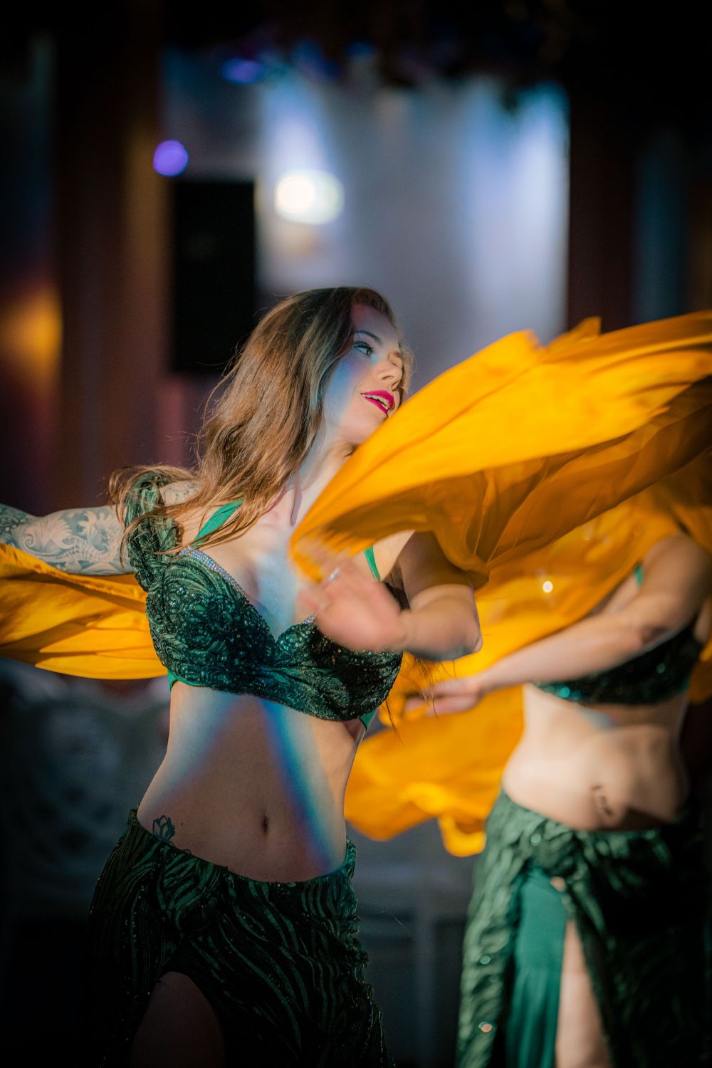 Bellydancer in emerald with a golden fan veil sweeping across the stage